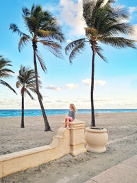 Full length of girl sitting by palm trees against beach