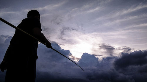 Low angle view of silhouette boy holding stick while standing against sky during sunset