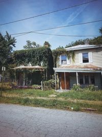 Plants growing on old building by field against sky