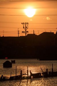 Silhouette sailboat on wooden post against sky during sunset