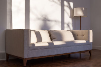 Light and shadows on wall of living room with beige linen modern couch and floor lamp