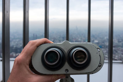 Close-up of man hand holding binoculars against sky