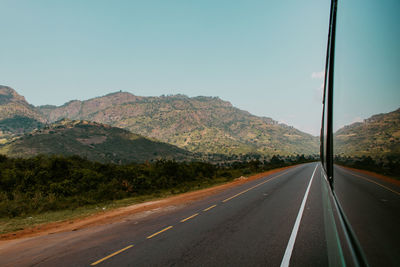 View of part of a bus and a road leading towards mountains against clear sky