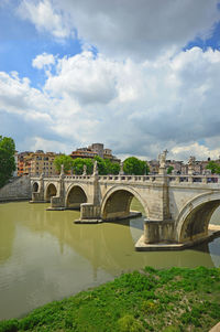 Arch bridge over river in city against sky