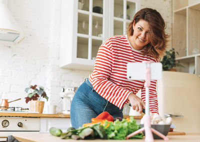 Gorgeous young woman plus size body positive records cooking process on phone camera at kitchen