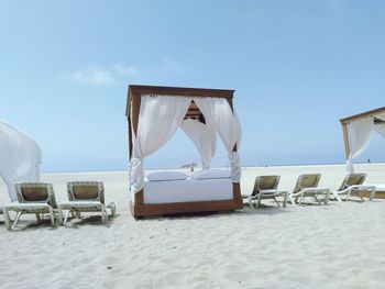 Deck chairs on beach against sky