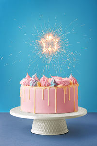 Close-up of birthday cake with sparkler on table against blue background