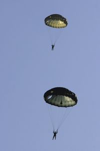 Low angle view of skydivers under parachutes against clear sky