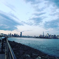 City at waterfront against cloudy sky