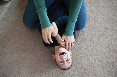 Midsection of mother tickling son on carpet at home