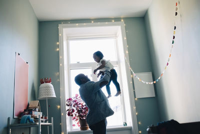 Side view of happy father holding daughter while standing by window at home