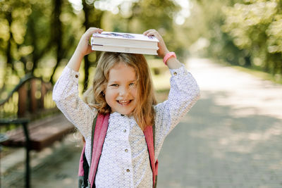 A charming little girl with a book on her head, on the first day at school or kindergarten. 
