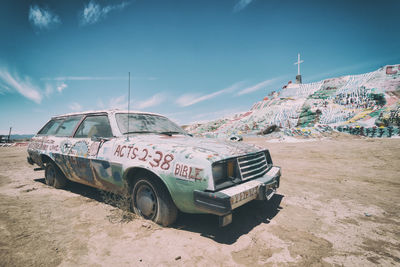 Abandoned car on land against sky