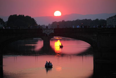 Silhouette people on bridge over river against sky during sunset