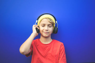 Boy listening music with headphones while standing against blue background