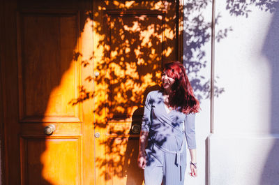 Smiling woman looking away while standing against wall outdoors