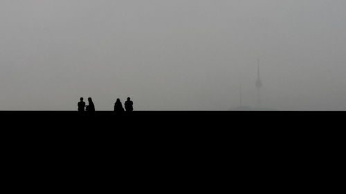 Silhouette people at beach against clear sky