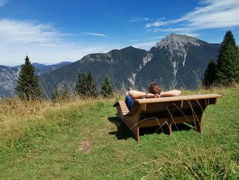 Man sitting on field against mountain range with blue sky in the background