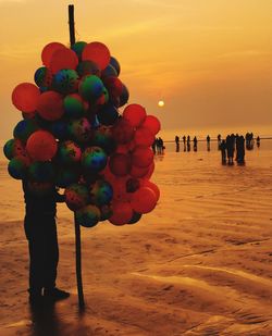 Multi colored balloons on beach against sky during sunset