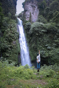 Man standing by waterfall in forest