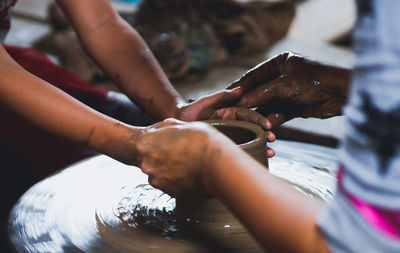 Cropped hands of people working on pottery wheel