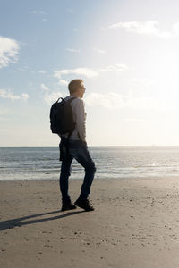 Rear view of man standing at beach against sky