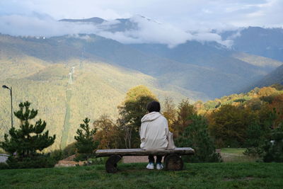 Rear view of man sitting on bench looking at mountains