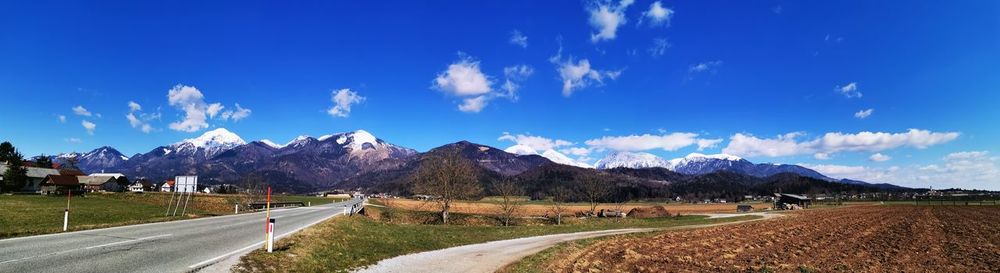 Panoramic view of road amidst field against blue sky