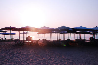 Parasols and chairs at beach against clear sky during sunset