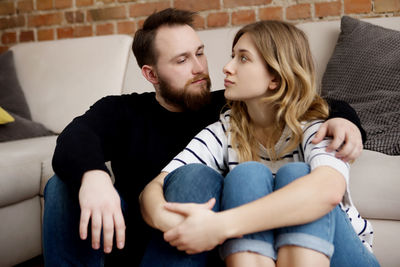 Young couple sitting by sofa at home