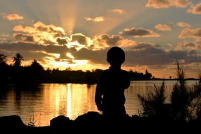 Silhouette man standing by lake against sky during sunset