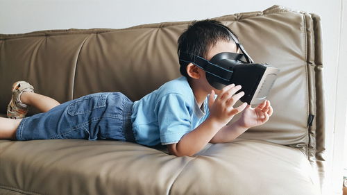 Boy using virtual reality simulator on sofa at home