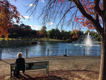 Rear view of man sitting by lake against sky