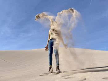 Full length of woman throwing sand while standing on desert