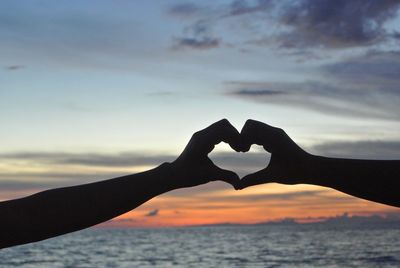 Silhouette hands of people making heart shape against sky during sunset