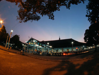 Illuminated street by buildings against sky at night