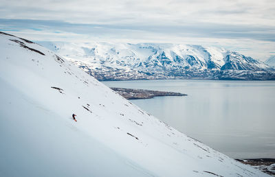 A man skiing down a mountain with snowy mountains and ocean behind