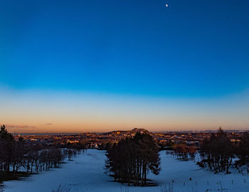 Snow covered field against sky during sunset