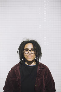 Portrait of smiling genderqueer person wearing eyeglasses standing against wall