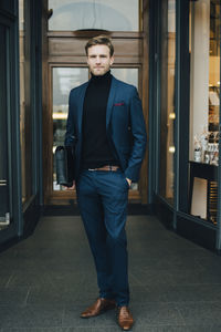 Portrait of businessman with hands in pockets standing by store in city