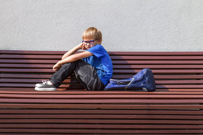 Side view full length of boy sitting against wall on bench