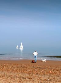 Rear view of man with dogs at beach against sky