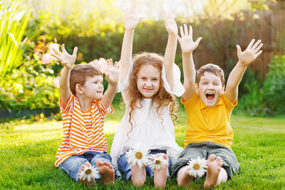 Happy friends children with daisy flowers at green grass in a summer park.