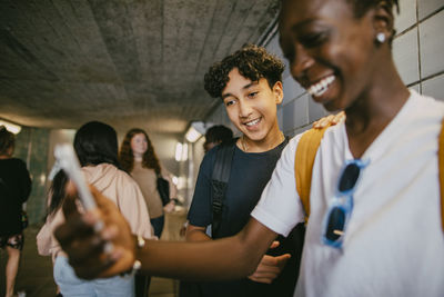 Smiling teenage boy standing with male friend using smart phone in underground tunnel