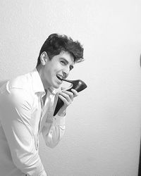 Young man with stiletto in mouth standing against white wall