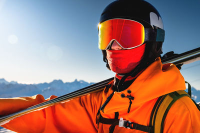 Portrait of a skier with skis on his shoulder. guy on a background of a mountain range on a sunny