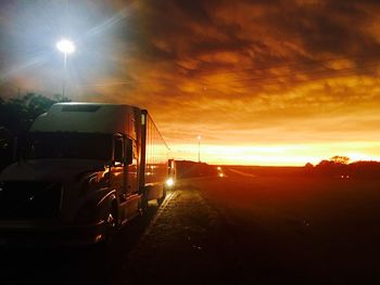 Cars on illuminated road against sky during sunset