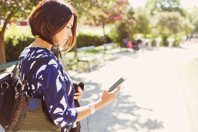 Side view of businesswoman using smart phone on footpath during sunny day