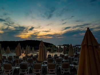 Chairs on beach against sky during sunset