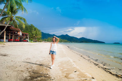 Portrait of smiling mid adult woman standing on beach against blue sky